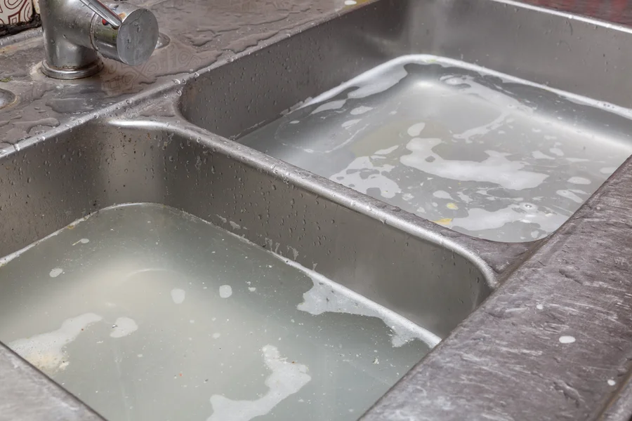 Standing water fills a double kitchen sink — clogged drain service near Lake Gaston Area