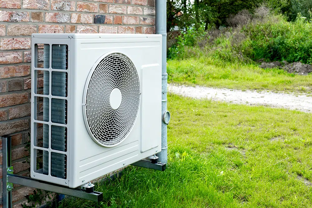 Compact mini-split outdoor unit mounted on brick home exterior — heat pump service Lake Gaston Area